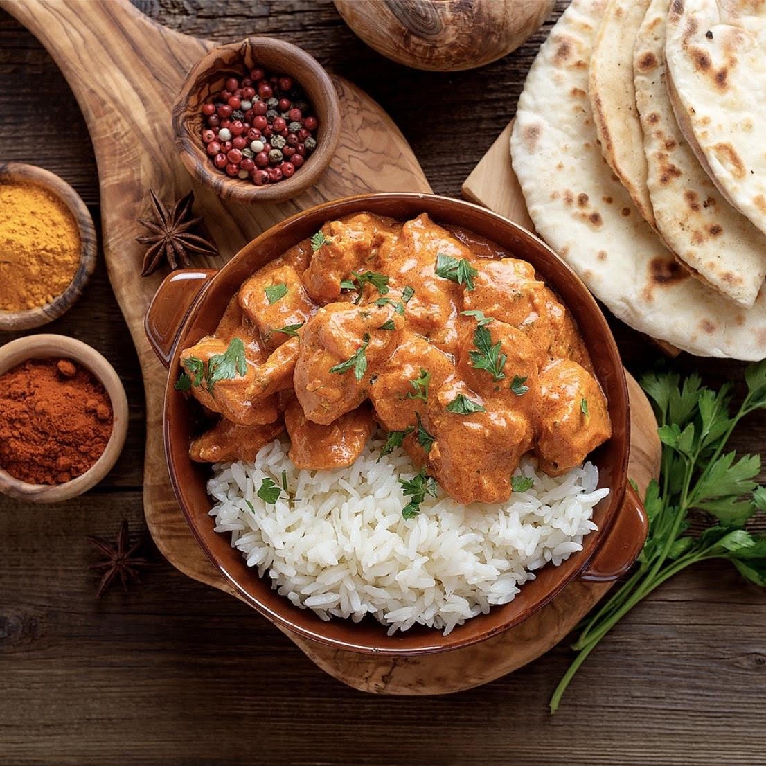 Rich and creamy Chicken Tikka Masala served over fluffy basmati rice with warm naan bread, finished with fresh cilantro and a drizzle of cream in a rustic bowl.